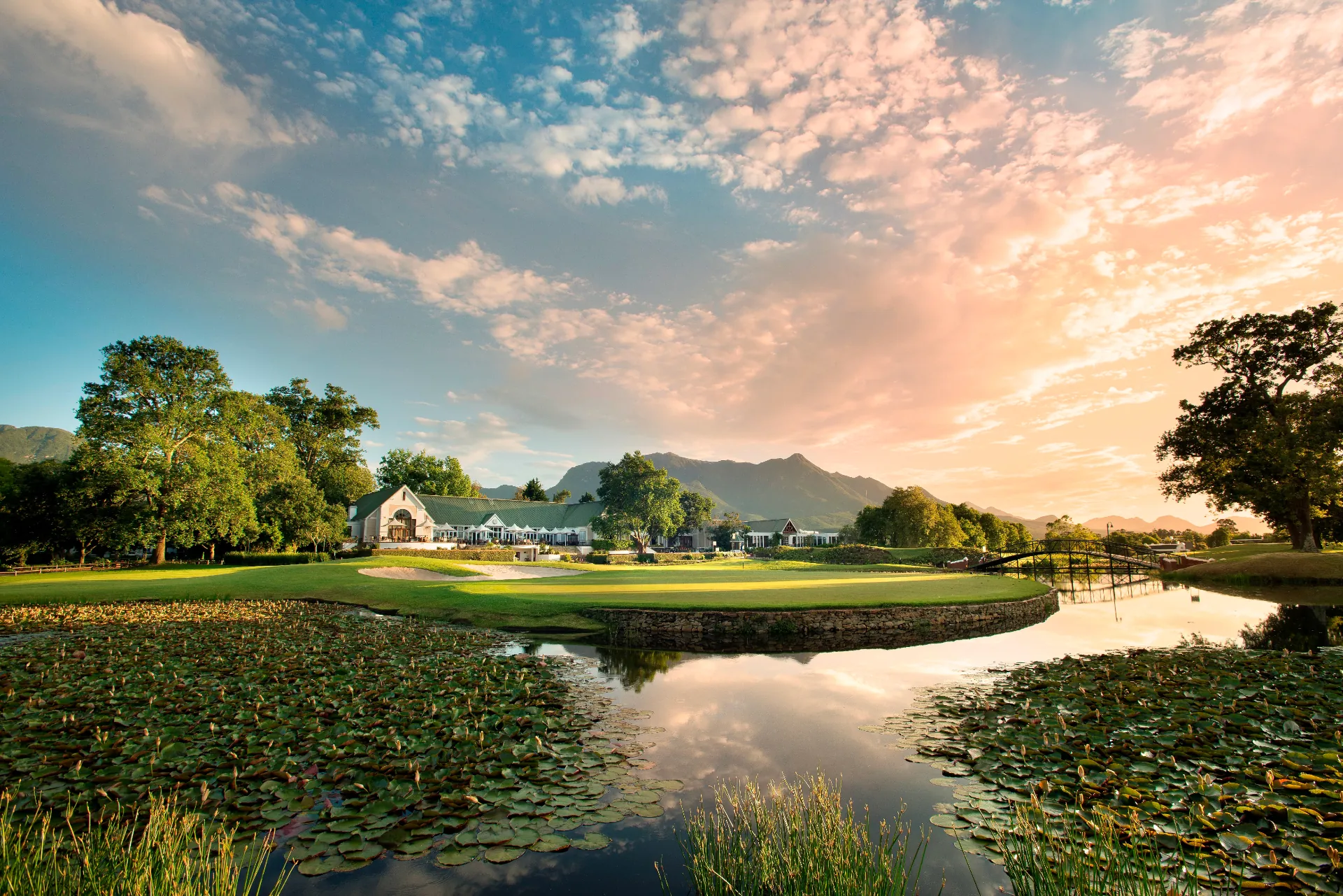 Golf estate and lake beneath South African mountains at sunset